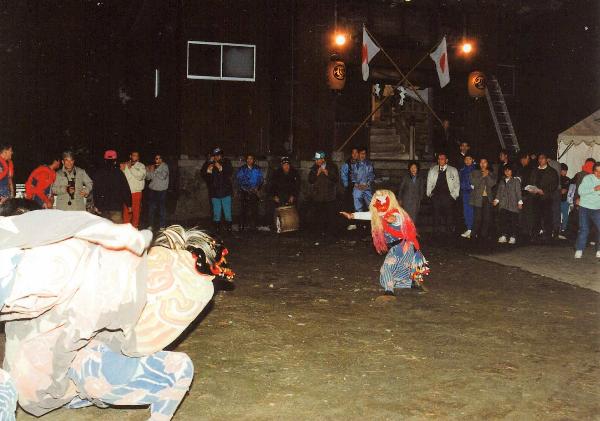 夜空の下、子供が獅子舞いを行っている写真。周辺には多くの人々が獅子舞いの様子を見守っている。