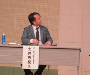 大きなスクリーンに目をやる土井秀紀氏の写真