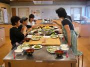 女性の先生が3人の小学生に料理を教えている教室の写真