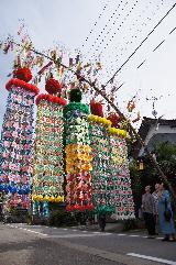 大きな竹に見事な5つの七夕飾りが下げられ道行く人が足を止めてそれを眺めている写真