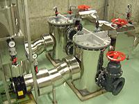 赤いバルブハンドルと配管が付いた2つの丸いアルミタンクの取水ポンプの写真