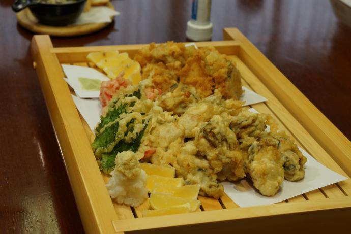 木製の四角い器に、様々な食材の天ぷらや牡蠣の天ぷらが載っている写真