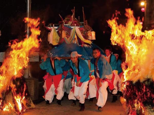 吉原恵比須祭りの最中の画像。道路の両脇には大きな炎が付けられており、炎に挟まれた道路を神輿を担いだ複数の男性が駆け抜けている。