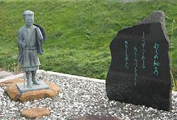 芝生を背景に左側に小さな松尾芭蕉の石像があり、右側には黒い石を削った石碑に、芭蕉の句が刻まれている記念碑の写真