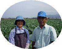 カリフラワー畑を背景に並んで写る、作業着姿の生産者ご夫妻の写真
