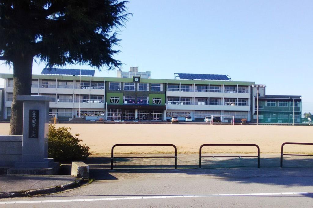 青空のもと校名が刻まれた門柱から望み、手前にはグランド、その向こうには緑の外壁がポイントで使われている黒東小学校の白い校舎の写真
