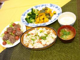 皿に盛られた肉団子料理、ブロッコリーと南瓜の料理、味噌汁、ヨーグルト、パエリアなどがテーブル上に並べられている写真