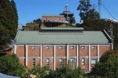 晴天の下、緑の木々に囲まれた薄緑の屋根にレンガ造りのどっしりと建つ水力発電所が美術館の写真