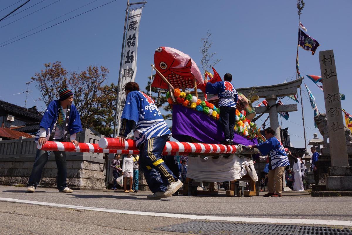 大きな鯛などの華やかな飾りを付けた屋形船を担いで練り歩く人々の写真