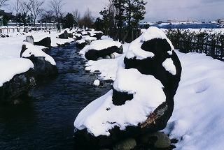 小川を挟んだ大小さまざまな岩に真っ白い雪が被った風景写真