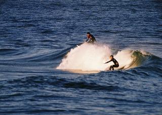 白波の中、黒いウエットスーツに身を包みサーフィンする二人の若者の写真