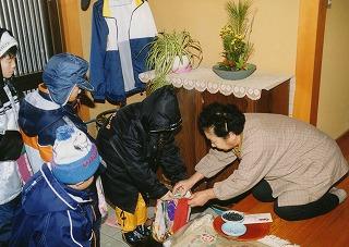 子どもたちが訪問した家の玄関で、家の女性から正月飾りを集め、菓子や米などをもらっている写真