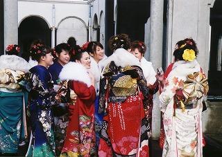 町民会館白壁の前で談笑する、色とりどりの晴れ着に身を包んだ女性たちの写真