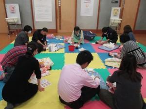5組みの参加者が人形の赤ちゃんを使って育児教室を行っている様子の写真